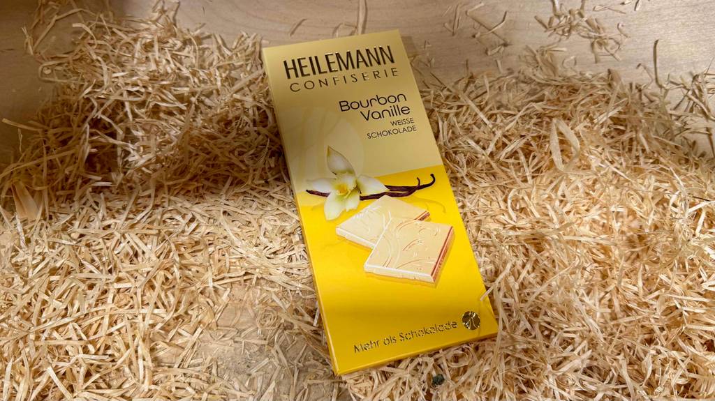 Eine weiße getestete Schokolade mit Bourbon-Vanille liegt in der Verpackung auf Holzspänen.