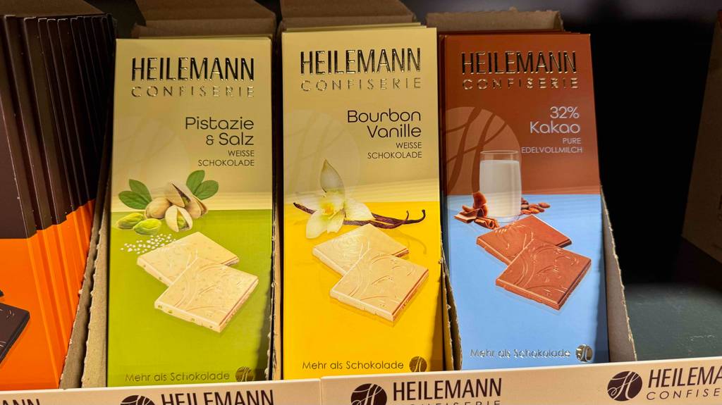 Eine weiße, getestete Schokolade in ihrer Verpackung steht in einem Verkaufskarton im Supermarktregal.