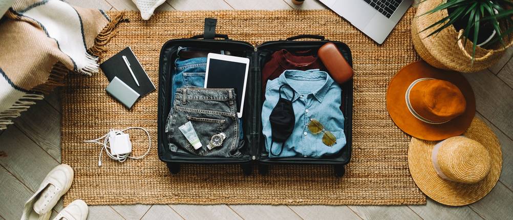 Geöffneter Koffer mit einsortierten Kleidungsstücken liegt auf dem Boden.