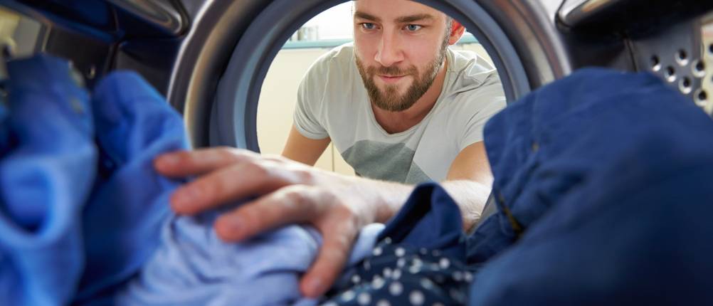 Mann räumt Klamotten in die Waschmaschine.