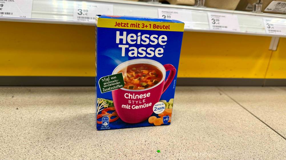 Vor einem Regal steht eine Packung der Heisse Tasse im Test auf dem Boden.