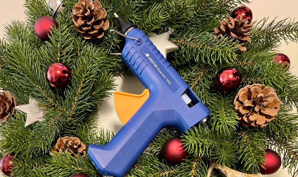 Steinel Gluematic 3002 liegt mittig in einem dekorierten Weihnachtskranz mit Kugeln, Zapfen und Tannenzweigen