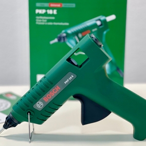 Die Bosch Heißklebepistole PKP 18 E steht schräg auf dem Tisch, daneben die grün-rote Verpackung mit Produktabbildung und technischen Details.
