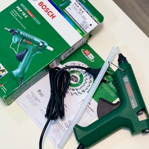 Die Bosch PKP 18 E liegt neben einem Netzkabel, Anleitung und aufgeschlagenem Karton. Die grüne Verpackung zeigt das Gerät auf der Vorderseite.