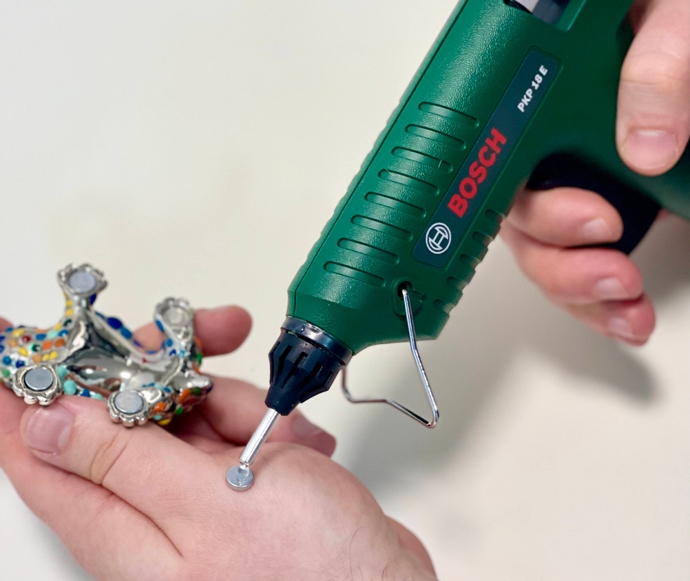 Die Bosch PKP 18 E Heißklebepistole wird verwendet, um einen kleinen Magneten auf eine runde Metallfläche zu kleben.