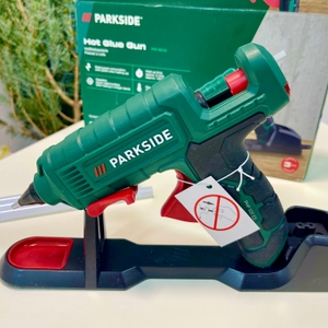 Parkside Heißklebepistole auf Ladestation vor Verpackung und Anleitung platziert.
