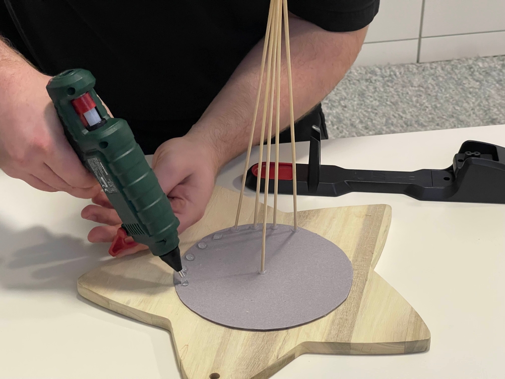 Parkside Heißklebepistole beim Kleben kleiner Punkte auf eine sternförmige Holzplatte mit Bastelstäben