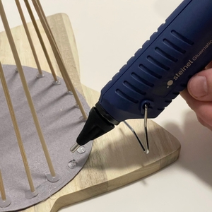 Steinel Gluematic 3002 trägt Heißkleber auf ein rundes Bastelholz mit Holzstäben auf