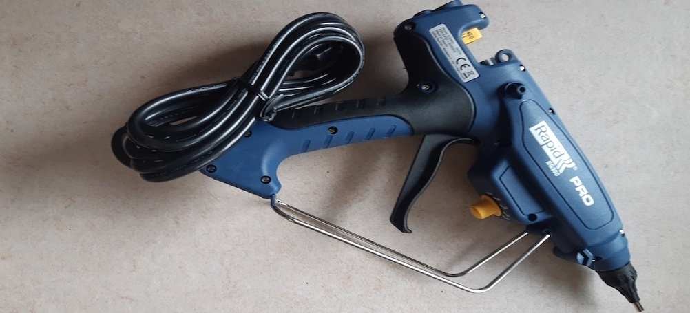 Heißklebepistole liegt mit aufgewickeltem Netzkabel auf hellem Untergrund