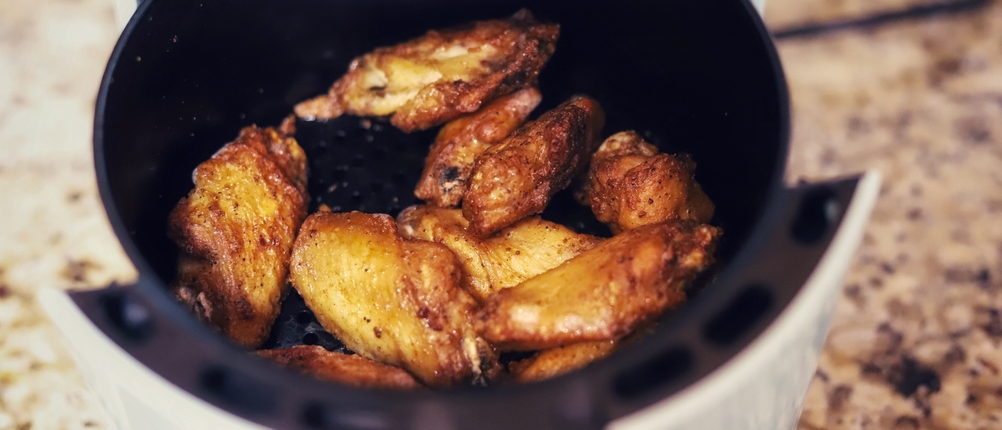 Hähnchenschenkel liegen in einer weißen Heißluftfritteuse.