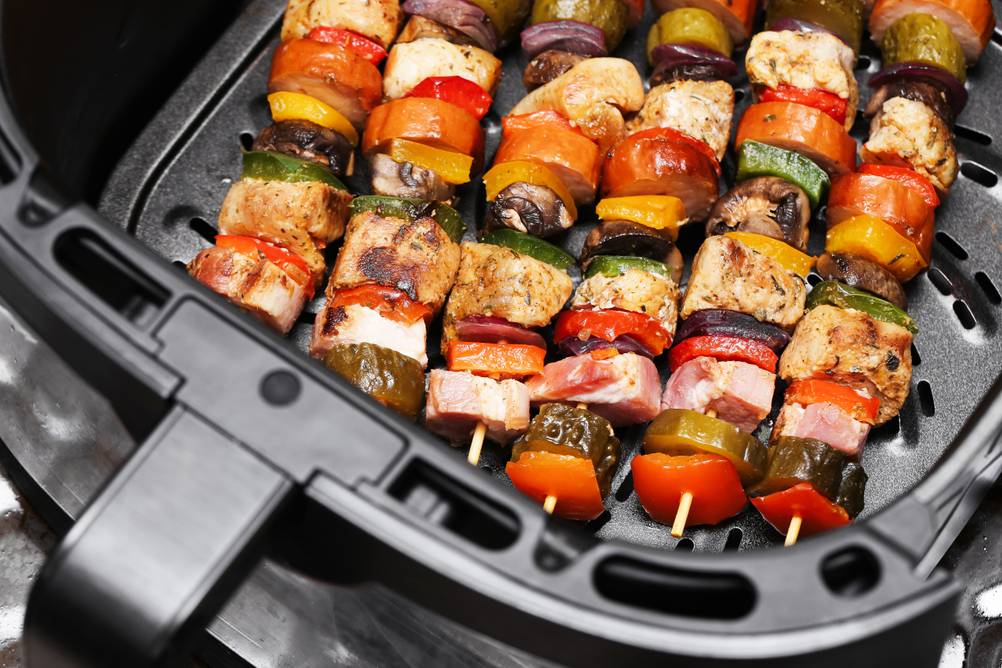 Im Heißluftfritteuse mit Grillfunktion Test werden Grillspieße gegart. Auf mehreren Spießen sind verschiedene Gemüsestücke, Pilze und Fleischstücke zu sehen. Insgesamt liegen 6 Spießen im Korb der Heißluftfritteuse.