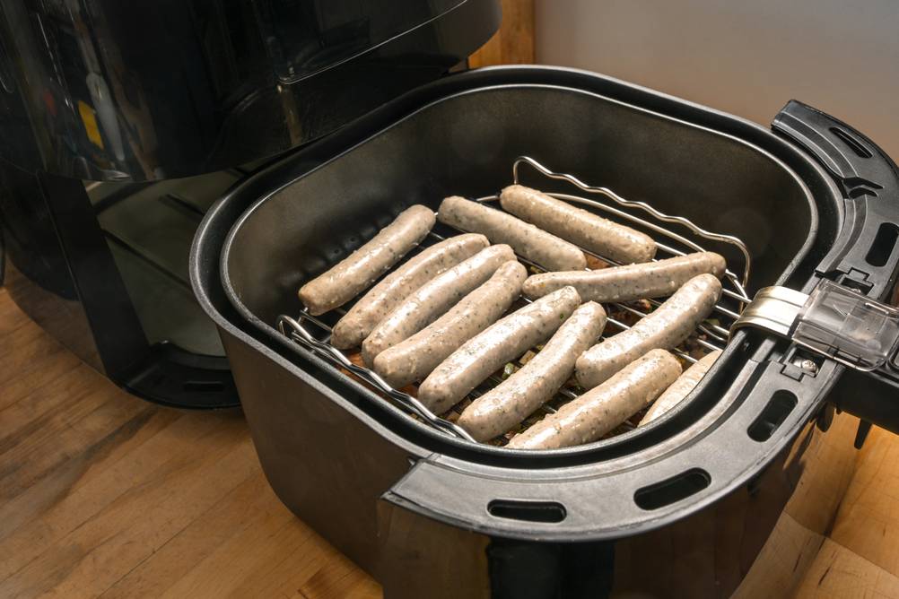 Kleine Nürnberger Würstchen liegen noch ungegart in einem Korb im Heißluftfritteuse-mit-Grillfunktion-Test. Die Würstchen liegen auf einem Gitterrosteinsatz