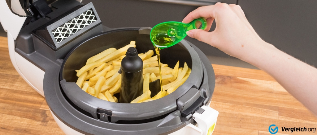 Heißluftfritteuse getestet: Einer Heißluftfritteuse mit Pommes wird vor der Zubereitung ein Löffel Öl zugefügt.
