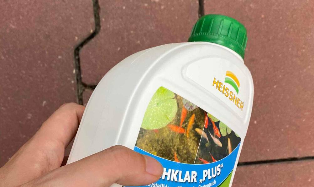 Detailansicht des grünen Schraubverschlusses einer weißen Kunststoffflasche mit getestetem Teichklar „Plus“ der Marke Heissner.