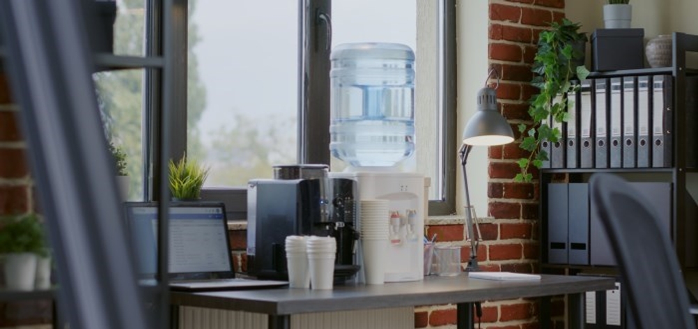 In einem Büro steht ein Wasserspender, daneben Becher, Aktenordner und ein Laptop.