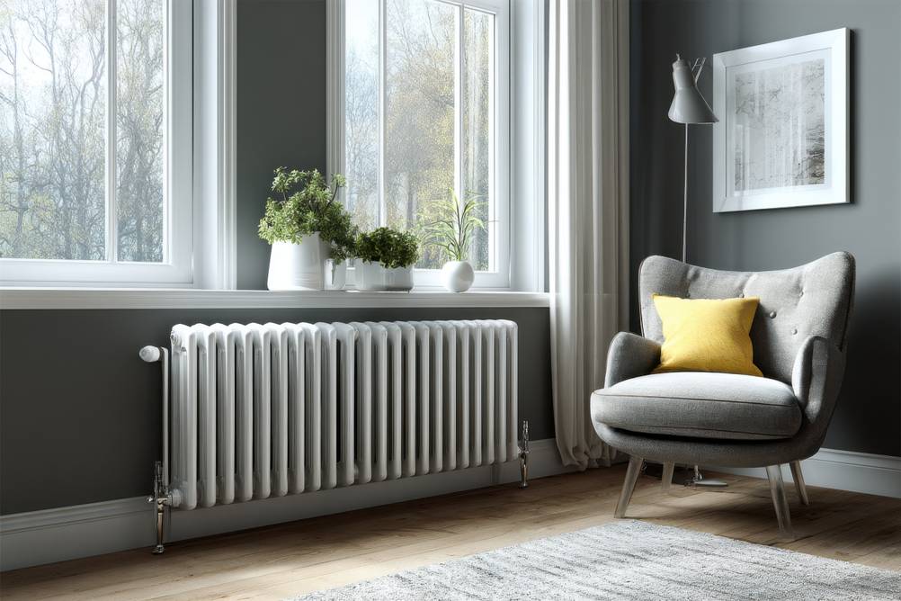 Heizkörper-Ventilator im Test: Ein Wohnraum mit großem Fenster links und großem Heizkörper; rechts ein Sessel mit Kissen.