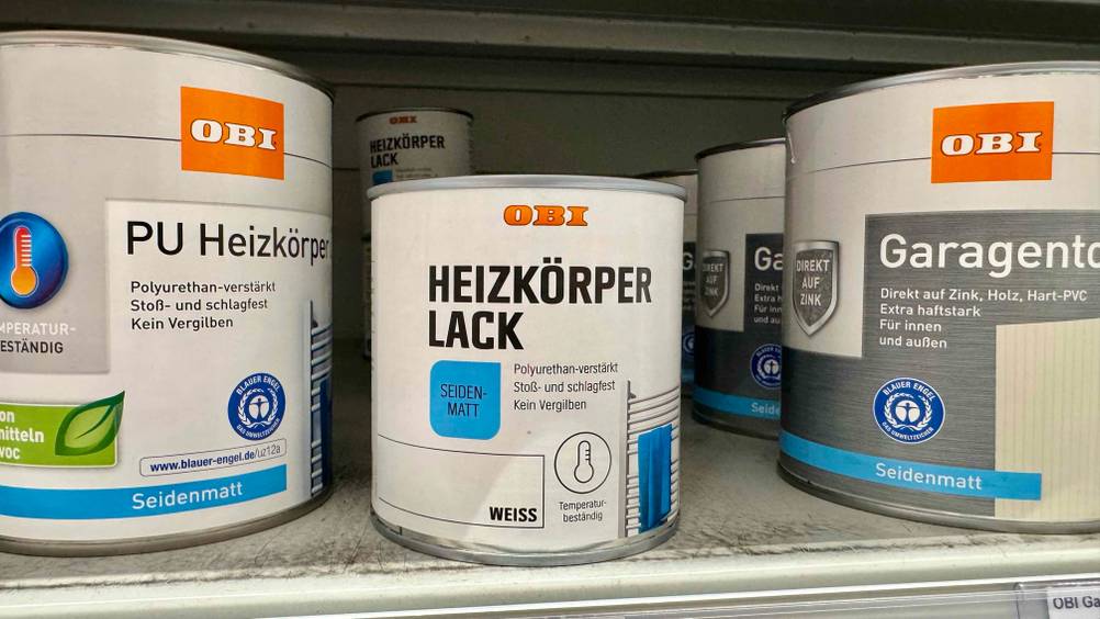 Mehrere Dosen des Heizkörperlack im Test neben anderen Produkten in einem Verkaufsregal.