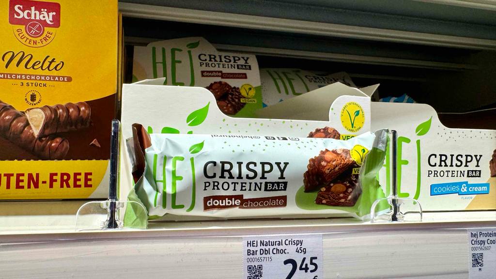 Vegane Proteinriegel im Test: Mehrere Riegel stehen hintereinander in einem Regal zwischen anderen Süßigkeiten.