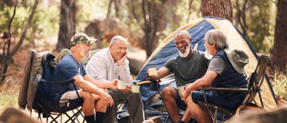 Helinox-Campingstuhl-Test: Eine Männergruppe auf Campingstühlen vor einem Zelt im Wald.