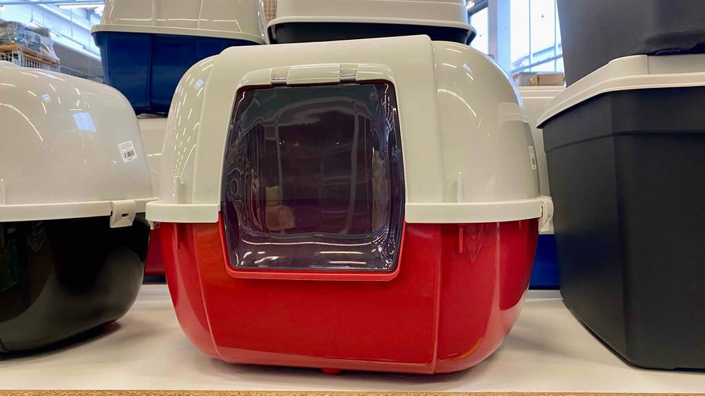 Katzentoilette-Test: Geschlossenes Modell mit roter Auffangschale, weißem Deckel und transparenter Eingangsklappe steht neben schwarz-weißen Katzentoiletten.