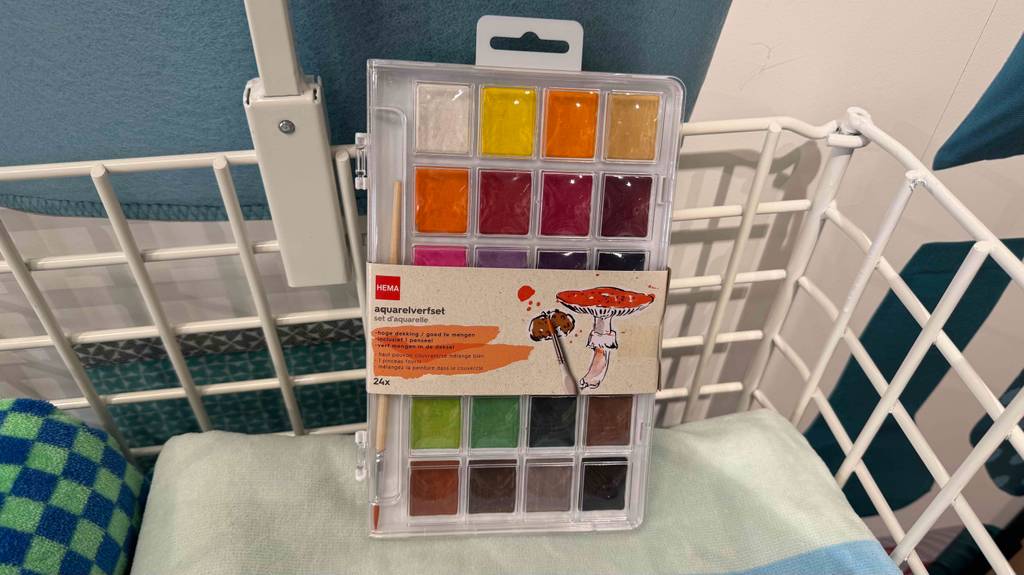 Die getesteten Aquarellfarben in einer transparenten Aufbewahrungsbox befinden sich in einem Verkaufskorb auf Handtüchern.