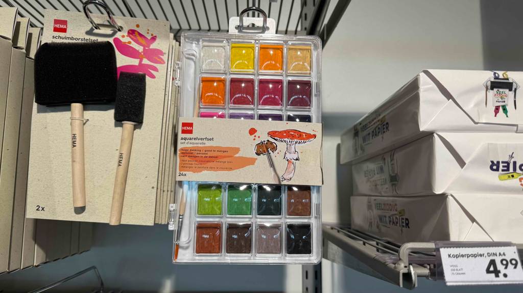 Im Test: Die Aquarellfarben in der transparenten Aufbewahrungsbox hängen an einem Verkaufsregal zwischen einem Borstenpinsel-Set und Kopierpapier.