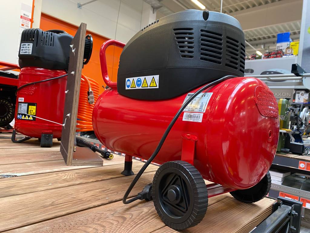 Ein roter 10-bar-Kompressor im Test steht auf einem Ausstellungsregal neben weiteren Kompressoren im Baumarkt.