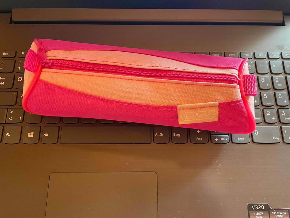 Ein geschlossenes rundes Federmäppchen liegt zum testen auf einer Tastatur.