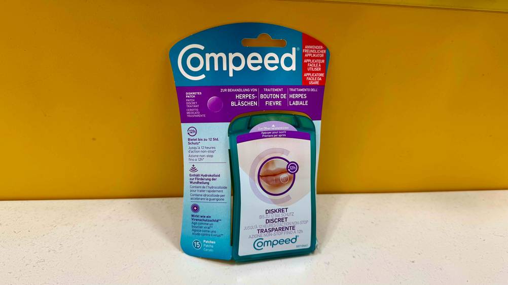 Eine Packung des Herpes-Mittels lehnt an einer gelben Wand.