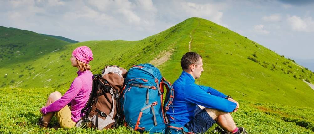 Reisetasche-mit-Rollen-Test: zwei Wanderer mit Rucksack, die Pause auf einer grünen Wiese machen