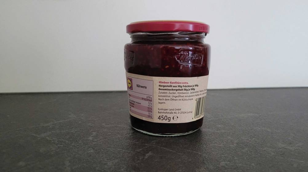 Himbeermarmelade getetet: Rückseite eines Glases der Marmelade auf einer dunklen Arbeitsplatte.