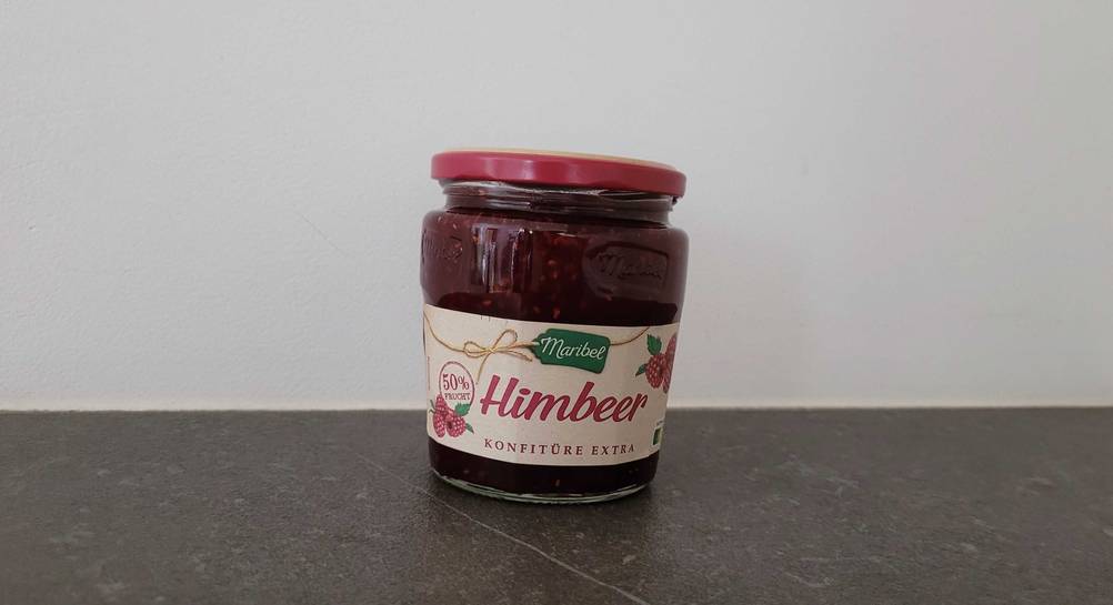 Ein Glas getestete Himbeermarmelade von vorne auf einer dunklen Fläche.