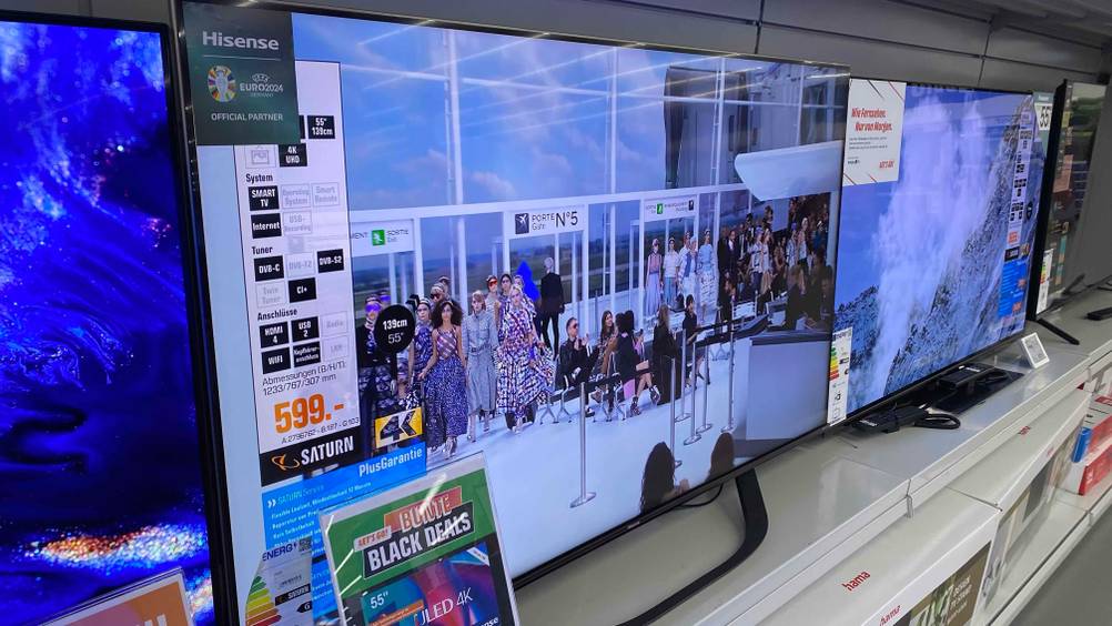 Hisense-TV 55 Zoll getestet: Ein Gerät von der linken Seite auf einem Verkaufsregal, im Hintergrund andere Geräte.