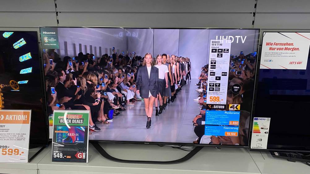 Ein getesteter Hisense-TV 55 Zoll von vorne in einem Verkaufsregal zwischen anderen Geräten und Preisangaben.