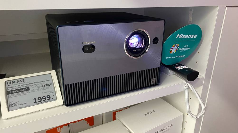 Im Test: Ein WLAN-Beamer in einem Verkaufsregal zwischen Fernbedienung und Preisschild.