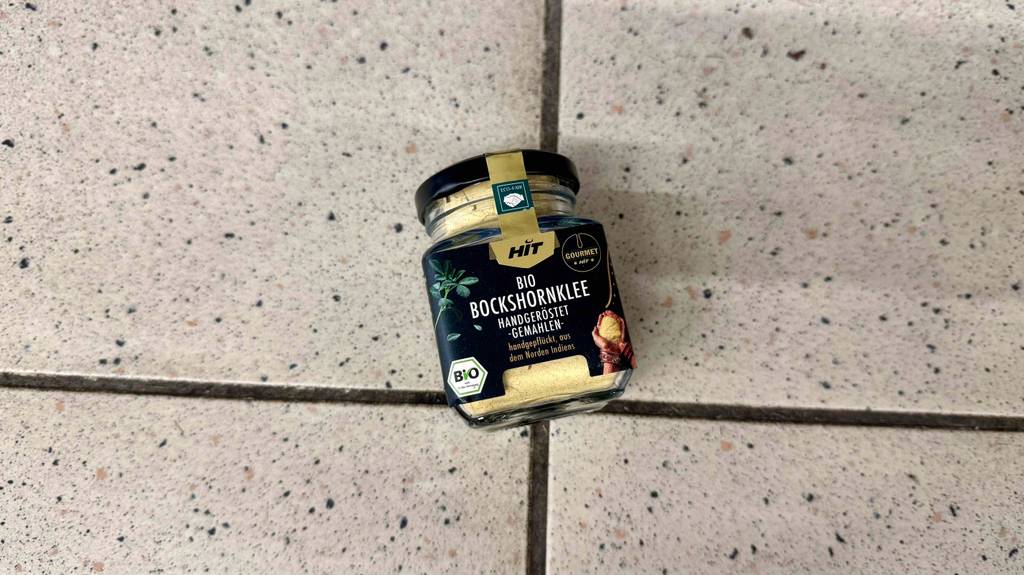 Getesteter Bockshornklee in Bio-Ausführung in der Glasdose mit Schraubverschluss liegt auf dem Boden.