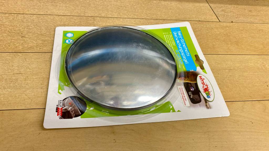 Getestet: ein Baby-Rückspiegel von Hits 4 Kids inklusive Verpackung auf einem Holzboden.