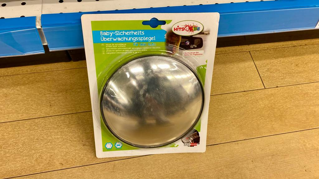 Im Test: ein Baby-Rücksitzspiegel der Marke Hits 4 Kids inklusive Verpackung lehnt an einem blauen Verkaufsregal.