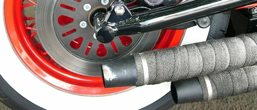 Hitzeschutzband-Test: Ein Auspuff mit einem Hitzeschutzband vor einem weiß-roten Reifen mit Scheibenbremse.