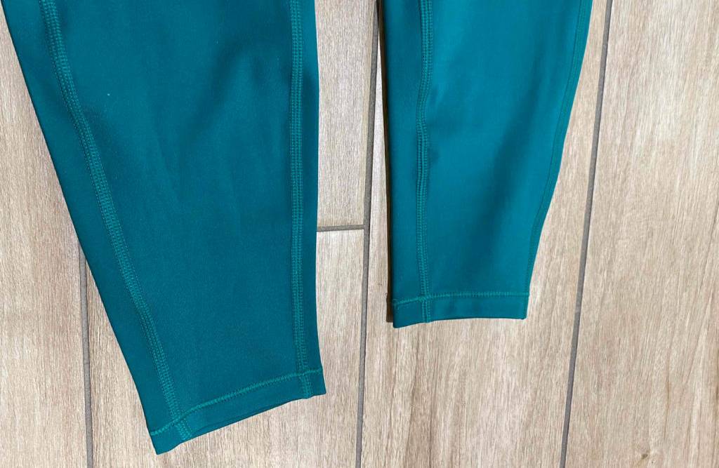 Detailansicht von türkisfarbigen Leggings im Test: untere Beinpartie mit Nähten auf Holzboden.
