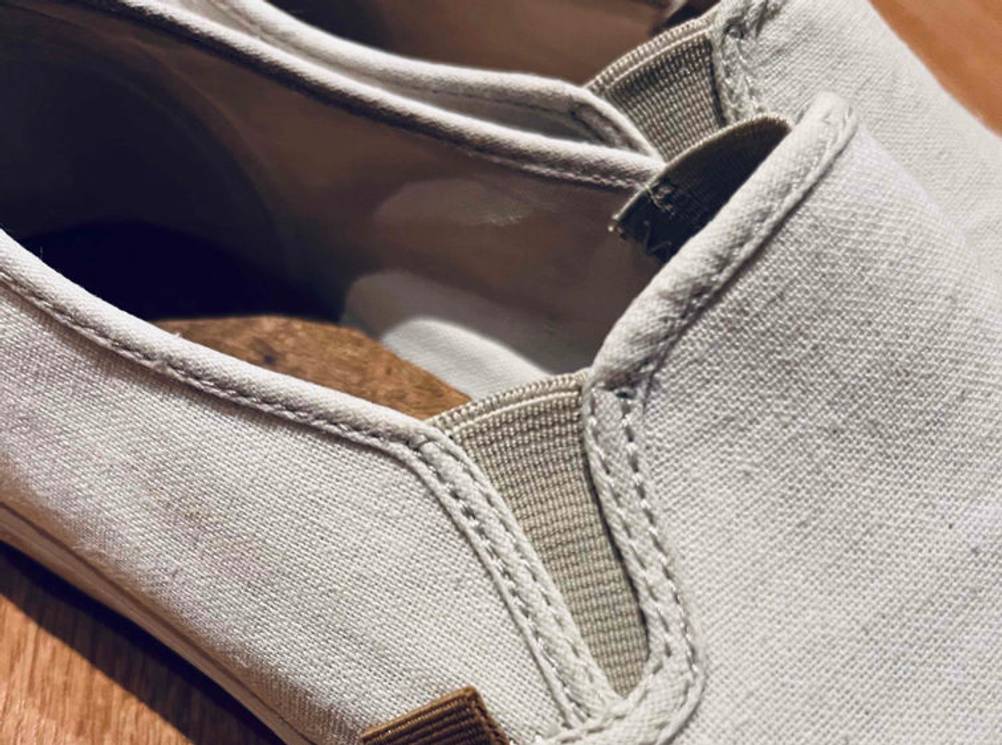 Nahaufnahme des Gummizugs im Schaftbereich von beigefarbigen getesteten Espadrilles für Herren auf einem Holzuntergrund.