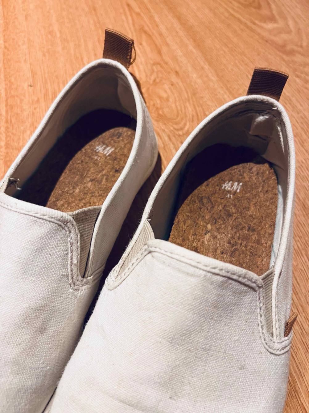 Beigefarbige H&M Espadrilles für Herren im Test stehen mit Fokus auf die Fersenlasche auf einem Holzboden.