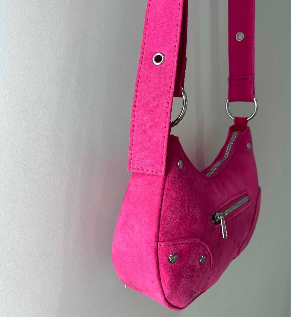 Umhängetasche für Damen-Test: Eine pinkfarben Umhängetasche für Damen inklusive verstellbarem Schultergurt, vor einer weißen Wand hängend.