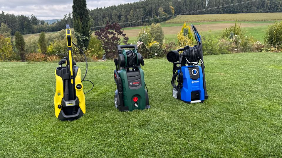 Drei Hochdruckreiniger stehen nebeneinander auf einer Rasenfläche
