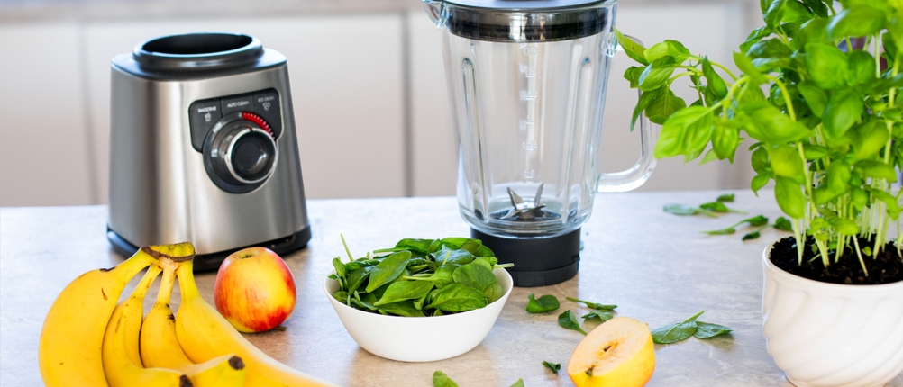 Hochleistungsmixer-Test: Hochleistungsmixer, Bananen, Äpfel und Basilikum sind auf einer Arbeitsfläche angeordnet.