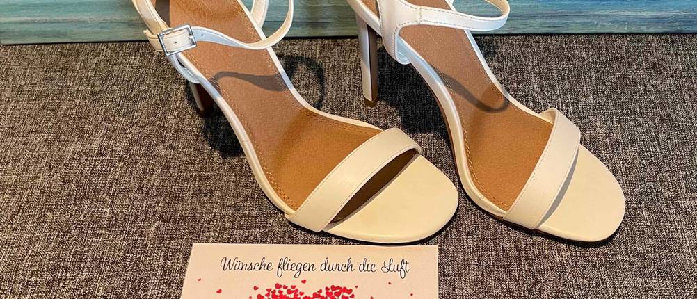 Weiße Hochzeitsschuhe im Test befinden sich vor einer Hochzeitskarte. 
