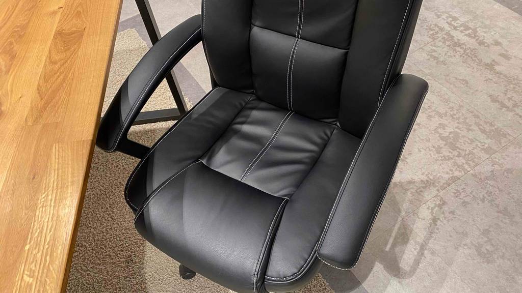 150-kg-Bürostühle-Test: Detailansicht von oben auf die gepolsterte Sitzfläche von einem schwarzen Modell mit weißen Ziernähten auf beigefarbenem Teppichboden.