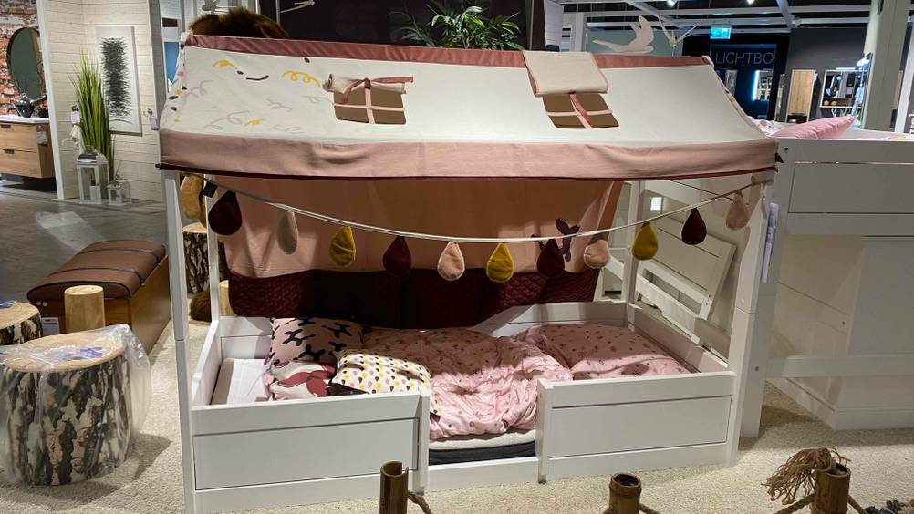 Hausbett getestet: Ein Bett in einer Möbelausstellung von vorne mit Girlande und rosa Bettwäsche.