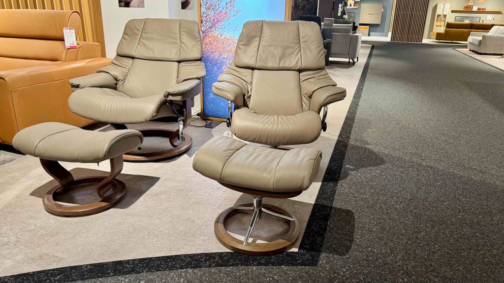 Zwei getestete Relaxsessel mit Hocker in beigefarbenem Design stehen nebeneinander im Möbelgeschäft.