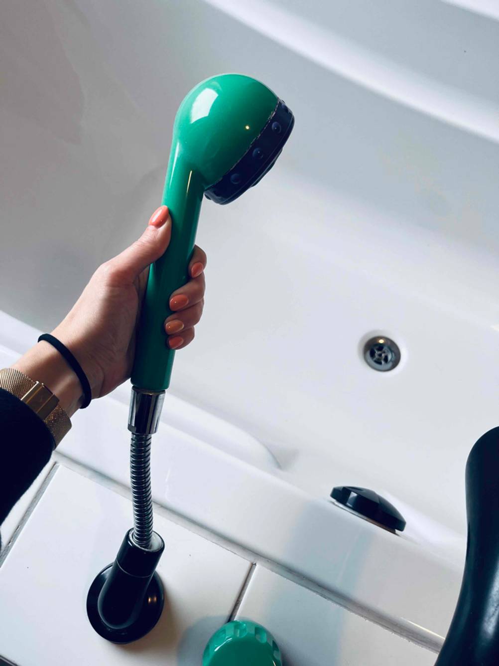 Hand hält einen grünen, ausziehbaren Duschkopf über eine Duschbadewanne im Test.